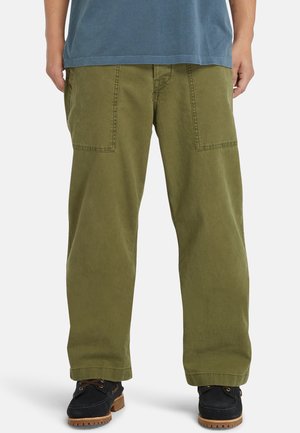 Olive green cotton cargo pants with a loose fit, featuring two large front pockets and visible stitching details. Worn with black shoes.