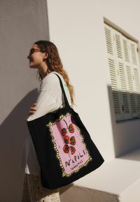 Black tote bag with a pink graphic featuring red tomatoes and the text "NAPOLI TOMATOES." Thick straps and canvas material.