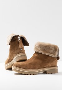 Bottines en daim marron avec semelles épaisses en caoutchouc et revers en fourrure pelucheuse, dotées de fermetures éclair argentées à l'arrière.