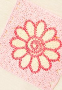 Geborduurd label met een roze bloem op een lichte achtergrond. De bloem heeft gele bloemenbladen omrand met roze met een golvende roze rand.