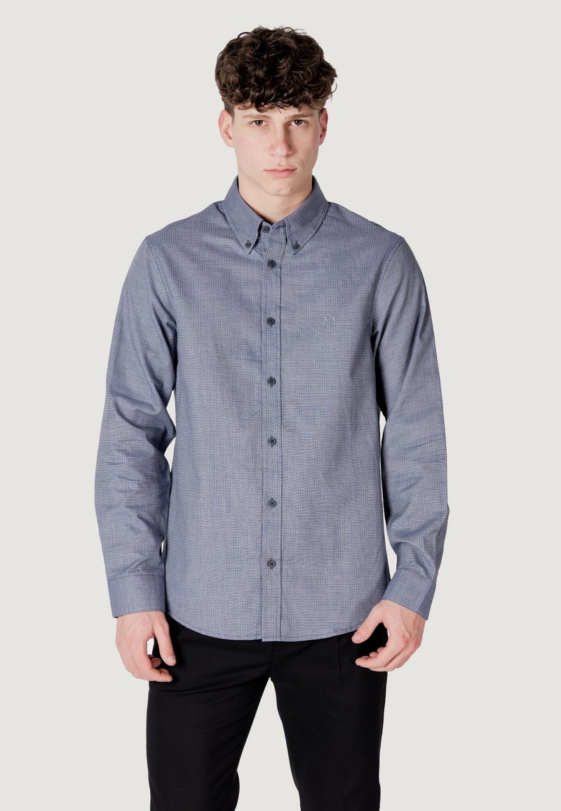 Camicia a quadri blu e bianca con colletto classico, maniche lunghe e bottoni scuri. Presenta un logo discreto sul petto.