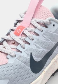Baskets de course Nike avec une tige bleu clair, des accents roses, un mesh texturé, des lacets blancs et un swoosh bleu foncé. La languette rose présente un motif floral.
