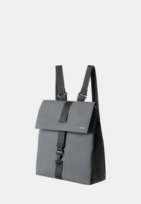 Sac à dos gris en matériau durable, avec un rabat repliable, des bretelles ajustables et une fermeture à boucle à l'avant. Design minimaliste.