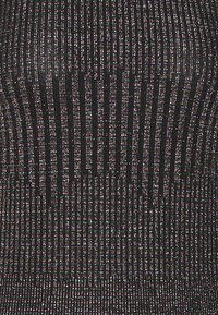 Svart plagg med vertikala, reflekterande trådar som skapar en texturerad yta. Mönstret består av tunna, glittrande ränder.