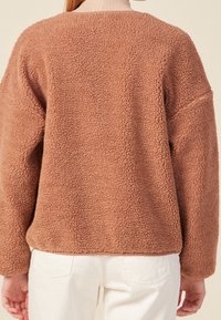 Hnědý huňatý fleecový svetr s kulatým výstřihem a dlouhými rukávy. Měkká textura, volný střih a minimalisticý design.