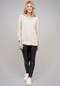 Pullover lungo a maniche lunghe color beige chiaro con scollo a V e maniche con polsini, abbinato a leggings neri e sneakers bianche. Tessuto piatto, vestibilità rilassata.