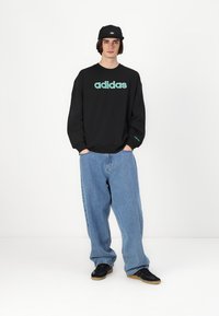 Sweatshirt preto com o logótipo "adidas" verde menta, combinado com jeans largos azuis claros e ténis pretos, além de um boné preto.