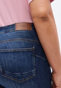 Τζιν παντελόνια σε σκούρο πλύσιμο με ραμμένη πίσω τσέπη και καφέ δερμάτινο ταμπελάκι με την επιγραφή "ONLY CARMAKOMA" στη μέση.