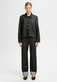 Black denim jacket with button closure and two front pockets, paired with matching black straight-leg pants and folded gray cuffs.