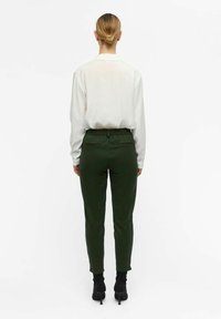 Un pantalon vert ajusté avec une taille élastique, associé à une chemise blanche à manches longues, présenté de dos sur un fond blanc.