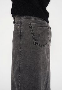 Falda de mezclilla gris, de cintura alta, con una forma ligeramente en A. Presenta dos bolsillos traseros y detalles de costura sutiles. Textura suave.