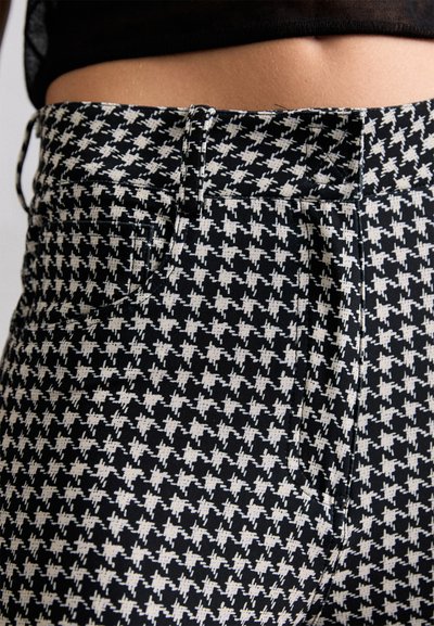 Mustriga must-valge houndstooth stiilis püksid, millel on liikuv disain, vöökoht, ees olevad taskud ja sile tekstuur.