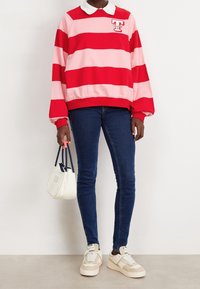 Sudadera a rayas rojas y rosas con un cuello blanco, combinada con jeans azules y zapatillas beige. Los accesorios incluyen un pequeño bolso blanco.