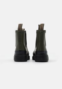 Bottines Chelsea en caoutchouc vert avec des panneaux latéraux élastiques, semelles texturées noires et languettes à l'arrière. Design simple et moderne.