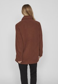 Brun fleecetrøje med høj krave, afslappet pasform og tekstureret stof. Har lange ærmer og en lige kant ved taljen.