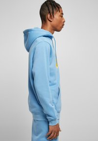 Felpa leggera azzurra con tasca a marsupio, polsini e orlo a costine. Presenta un logo giallo sul petto e un cordino in blu a contrasto.