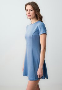 Robe à manches courtes, en forme de A, en tissu doux et léger bleu clair avec un col rond et des panneaux latéraux sans couture, présentant une texture lisse et une coupe décontractée.