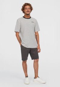 Gestreept t-shirt met korte mouwen in wit en zwart, gecombineerd met donkergrijze shorts. Witte sneakers maken de casual look compleet.
