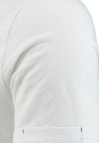 Nahaufnahme eines weißen Kurzarmhemdärmel mit sichtbarer Naht und rotem Fadendetail am Bündchen.