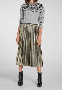 Grå stickad tröja med svart mönstrad ok, kombinerad med en glansig, plisserad guldkjol och svarta ankelstövlar.