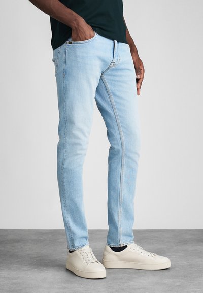 Jeans in denim azzurro chiaro con una vestibilità slim, design a cinque tasche e cuciture a contrasto, abbinati a sneakers bianche basse.