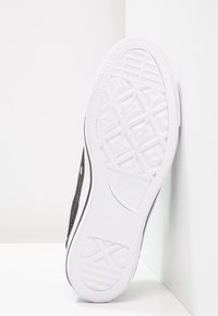 Czarny sneaker z teksturowaną cholewką, białą gumową podeszwą z geometrycznym wzorem bieżnika oraz czarnymi bocznymi akcentami.