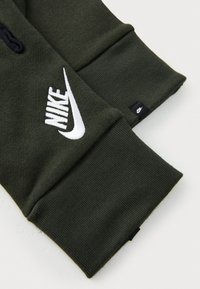 Sötétzöld kapucnis pulóver anyag ribbelt ujjal, fehér hímezett Nike logóval és egy kis fekete Nike címkével az oldalán.