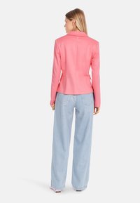 Pink tailored blazer with a single button detail, smooth texture, and fitted shape, paired with loose light blue jeans.