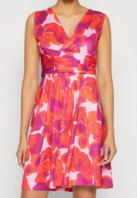 Robe fleurie rose, avec de grands motifs floraux rouges et violets, col en V, corsage ajusté et jupe évasée.