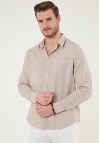 Helle beige Langarm-Hemd mit Knopfleiste aus strukturiertem Stoff. Mit einer Brusttasche, spitzem Kragen und abgerundetem Saum.