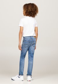 Plave traperice uskog kroja s dva stražnja džepa i kožnom oznakom branda. Uparene s bijelom majicom i bijelim tenisicama.