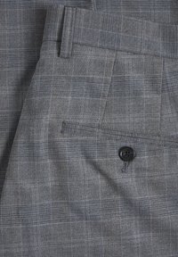 Šedá látka s károvaným vzorem obsahuje jemnou mřížkovou strukturu v odstínech modré a hnědé. Součástí je zadní kapsa s černým knoflíkem.