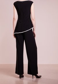 Svart ärmlös topp med en svängd nederkant och vit accent, ihop med svarta vida byxor. Slät tyg, stilren design, bärs med klackar.