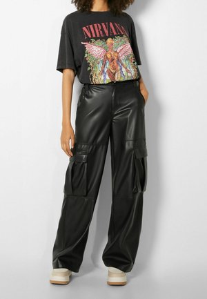 Persona che indossa una maglietta nera dei Nirvana con una grafica colorata di un angelo, pantaloni cargo neri a gamba larga e sneakers bianche con piattaforma.