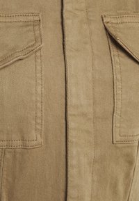 Brun bomullsskjorta med två bröstfickor, synlig sömnad, rak skärning och mjuk textur. Tyget verkar hållbart med en lätt lyster.