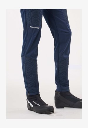 Granatowe spodnie narciarskie z pikowanymi akcentami, wyposażone w boczny zamek i detal z logo. W zestawie z czarnymi butami narciarskimi o smukłym profilu.
