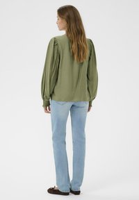 Blouse vert olive avec des manches bouffantes et des poignets élastiques, associée à un jean droit bleu clair et des ballerines marron foncé.