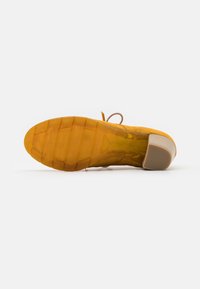 Sole di scarpa in suede giallo con grip in gomma testurizzata, punta arrotondata e tacco di colore chiaro a contrasto. Presenta lacci nella parte superiore.
