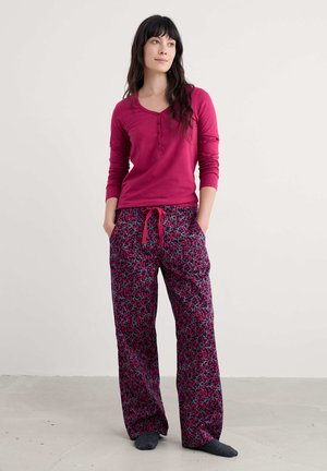Fuchsia lange mouw top met een henleyhalslijn en drie knopen, gecombineerd met wijde roze broek met bloemenpatroon en een trekkoord in de taille.