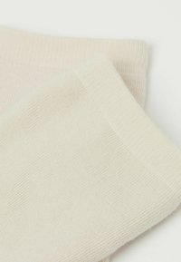 Calzini di cotone beige con bordo a costine e texture liscia. Il tessuto appare morbido e flessibile, con un design senza cuciture.