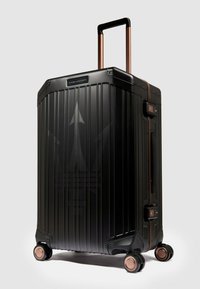 Schwarzer Hartschalenkoffer mit vertikalen Rillen, roségoldenen Akzenten, ausziehbarem Griff und vier Rollen für einfache Mobilität.