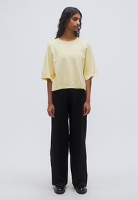 Sweat-shirt jaune court avec manches larges, associé à un pantalon noir à jambes larges. Les tissus semblent doux et texturés avec une coupe décontractée.