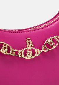 Petit sac en cuir rose vif avec fermeture éclair dorée et chaîne décorative dorée ornée d'initiales entrelacées sur le devant.