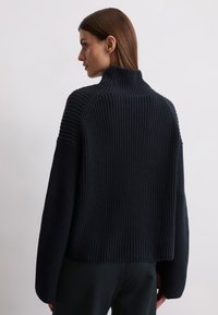 Dark navy knitted sweater with a high collar, ribbed texture, and dropped shoulders. Features a relaxed fit and short, cropped length.