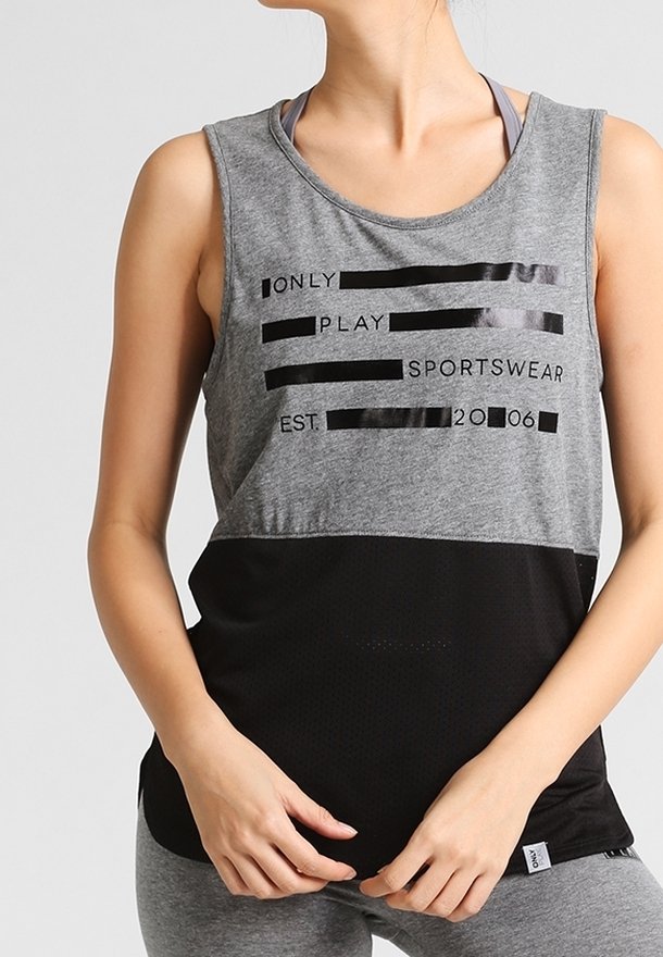 Woman wearing grey and black sleeveless sports top with text "ONLY PLAY SPORTSWEAR EST. 2006" standing with hands clasped at waist.