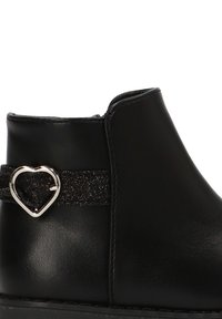 Botas negras hasta el tobillo con un acabado de cuero suave, que cuentan con una banda negra texturizada adornada con una hebilla en forma de corazón plateada.