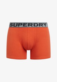 Boxer shorts naranjas de algodón con una cinturilla elástica gris que presenta el nombre de la marca "SUPERDRY" en letras negras.