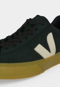 Baskets basses noires avec logo V blanc sur le côté et semelle épaisse en caoutchouc jaune, avec des lacets noirs et une semelle extérieure texturée.