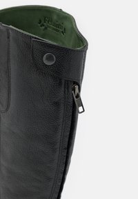 Botte noire en cuir texturé avec zip latéral et bouton-pression, doublure intérieure en daim vert et nom de la marque embossé à l'intérieur du haut.