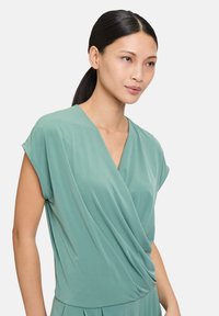 Haut enveloppant à manches courtes aqua avec un décolleté en V et un tissu drapé pour une texture douce, assorti d'une partie inférieure plissée.